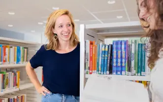 Vrouw korter blond haar en vrouw bruin haar krullen bij boekenrek