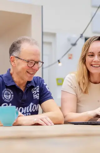 Oudere man en studente aan tafel op laptop atrium